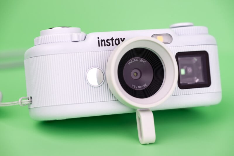 A white Instax digital camera with a 28mm F2.2 lens sits on a solid green background.