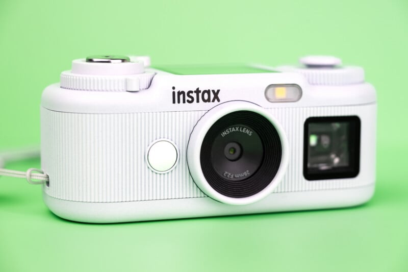 A white Fujifilm Instax Pal digital camera sits on a solid light green background.