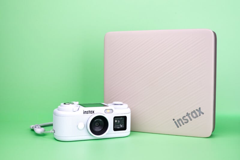 A white Instax digital camera sits next to a beige, rectangular Instax-branded case against a solid light green background.