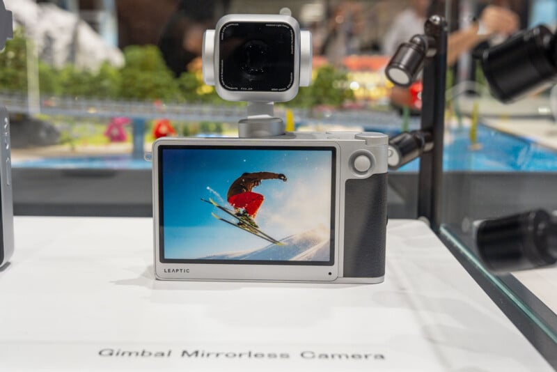 A silver LEAPTIC gimbal mirrorless camera sits on a white display surface, showing a skier on its screen.