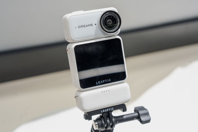 A white, modular action camera with a screen labeled "LEAPTIC" is mounted on a tripod stand against a plain background.