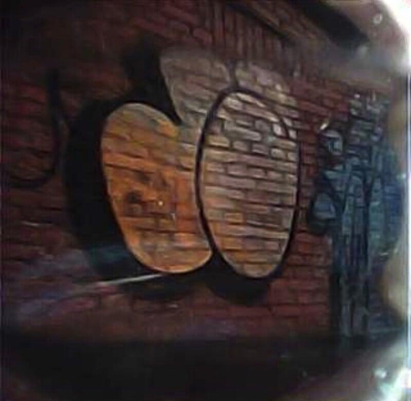 A brick wall features a large, stylized graffiti mural with two prominent, rounded shapes outlined in black, set against a dark, textured background.
