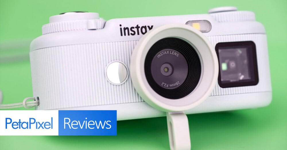 A white Instax digital camera sits on a solid green background, with a PetaPixel Reviews logo in the bottom left corner.