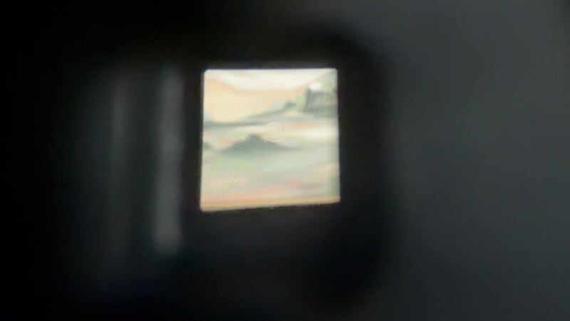 A view through a camera viewfinder showing a blurry, out-of-focus landscape with a central circular focus point.
