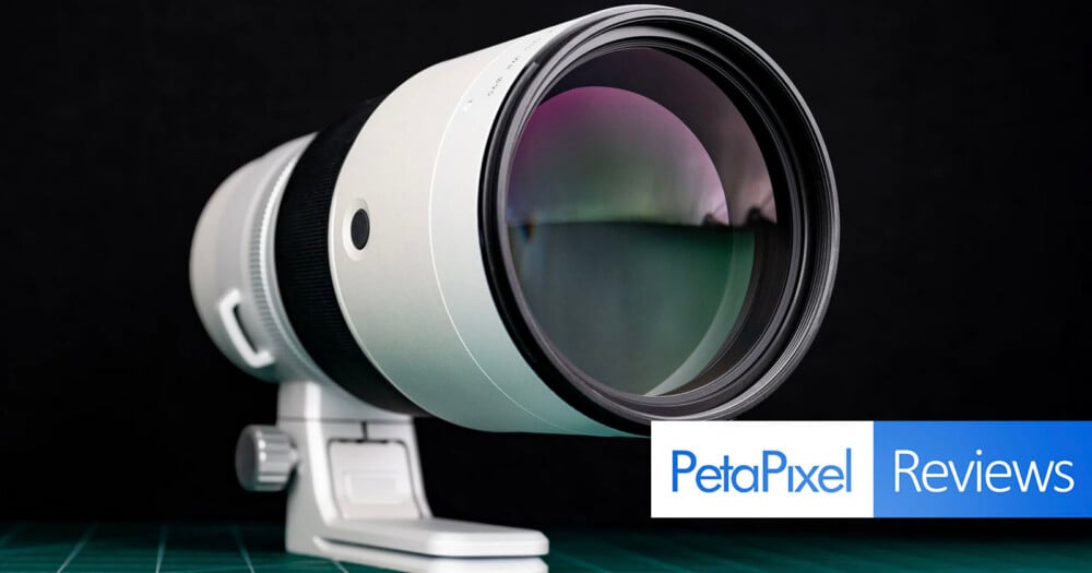 A white telephoto camera lens sits on a green cutting mat against a black background, with a PetaPixel Reviews logo in the corner.