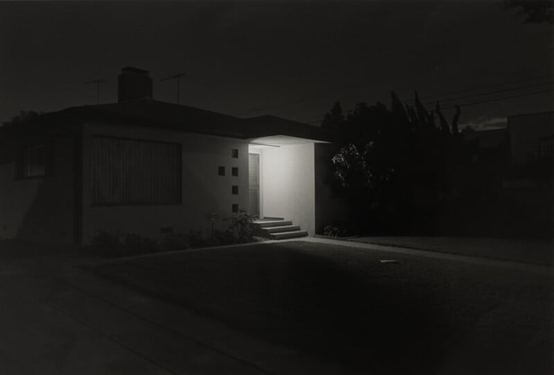 A single-story house at night with a brightly lit entryway contrasting against the dark, shadowed exterior.