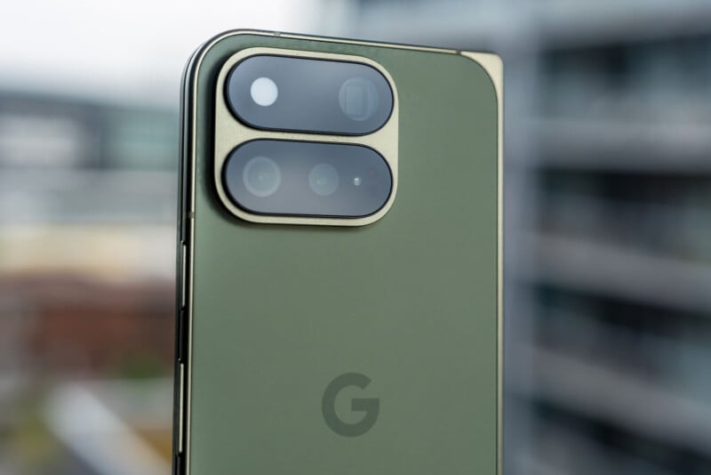 A close-up view of the back of an olive green smartphone featuring a prominent, pill-shaped camera module with two lenses and a flash, and a Google "G" logo centered below.