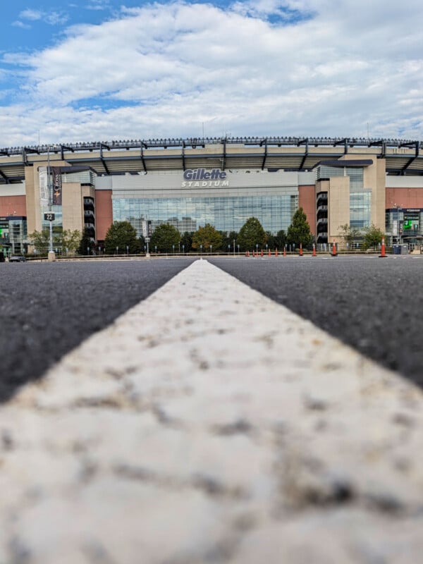 A low-angle view of Gillette Stadium from a parking lot, with a white painted line leading toward the building entrance.