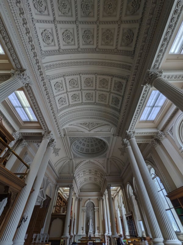 A low-angle view of a grand, neoclassical interior featuring a high, coffered vaulted ceiling, ornate Corinthian columns, and a central dome.