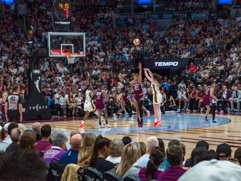 Two basketball players jump to contest a shot near the basket during a game in a crowded arena.