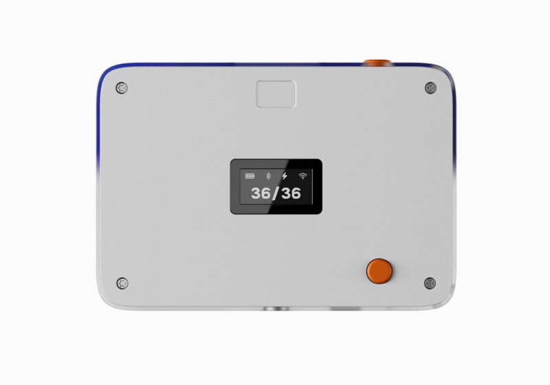 A rectangular, light gray electronic device with a small digital display showing "36/36" and status icons, featuring an orange circular button and four corner screws.