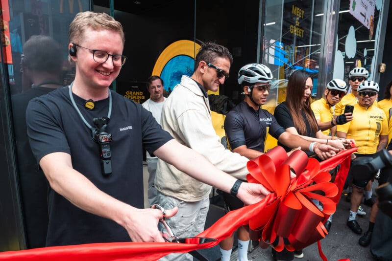 A group of people, including Casey Neistat, cut a large red ribbon during a store opening event.