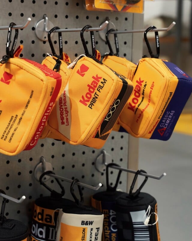Small, rectangular pouches designed to look like vintage Kodak film boxes hang from metal hooks on a pegboard display.