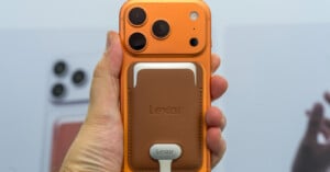 A hand holds an orange smartphone with a brown leather magnetic wallet attached to the back, featuring a Lexar logo and a connected white cable.