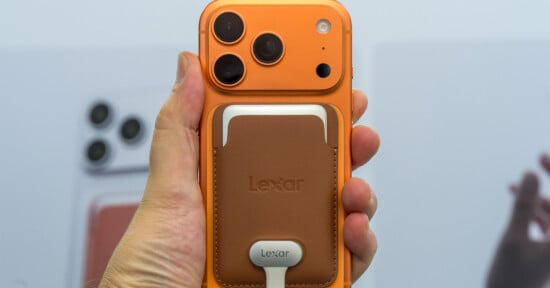 A hand holds an orange smartphone with a brown leather magnetic wallet attached to the back, featuring a Lexar logo and a connected white cable.