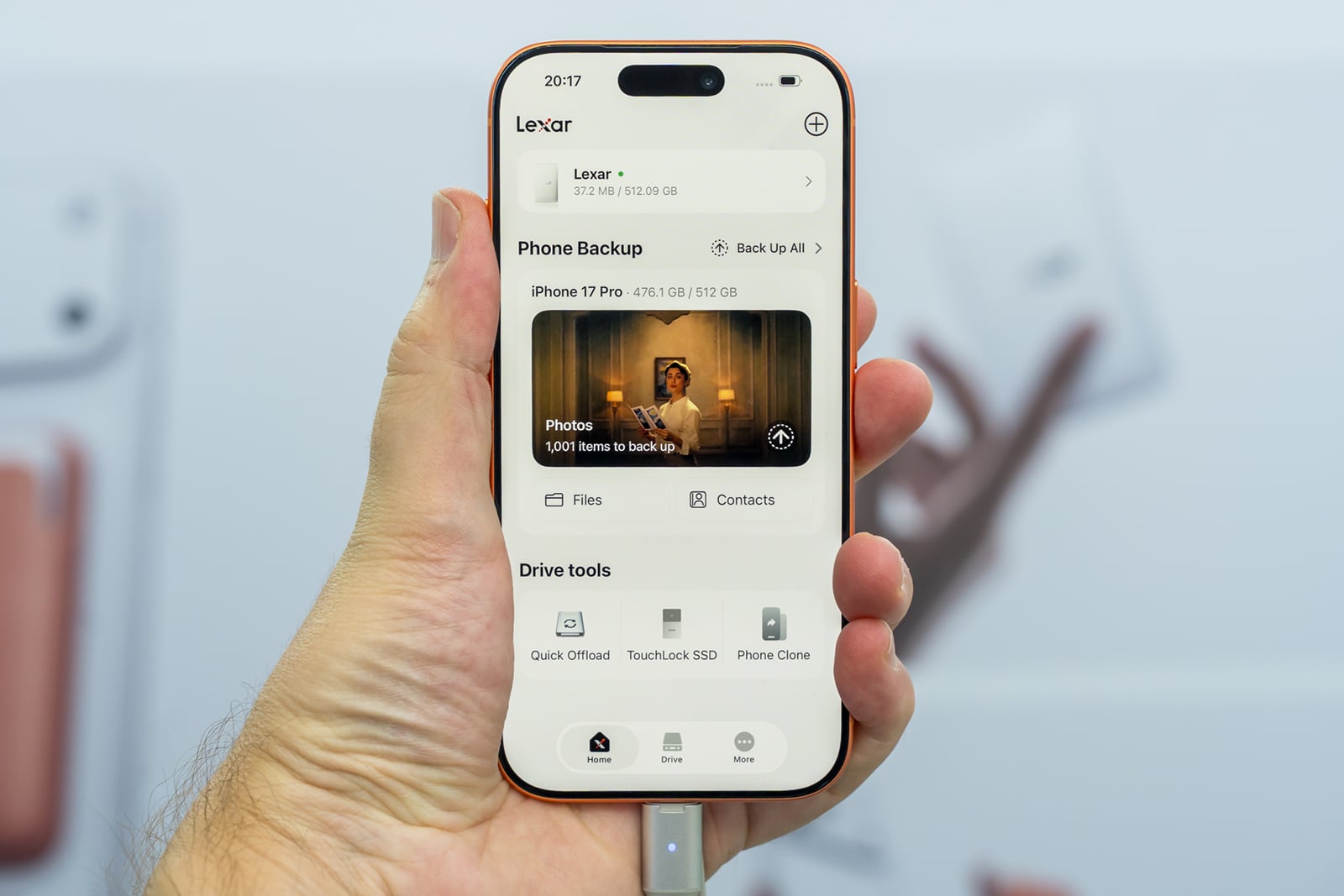 A hand holds an orange smartphone displaying the Lexar app interface, which shows storage usage, backup options, and drive tools.