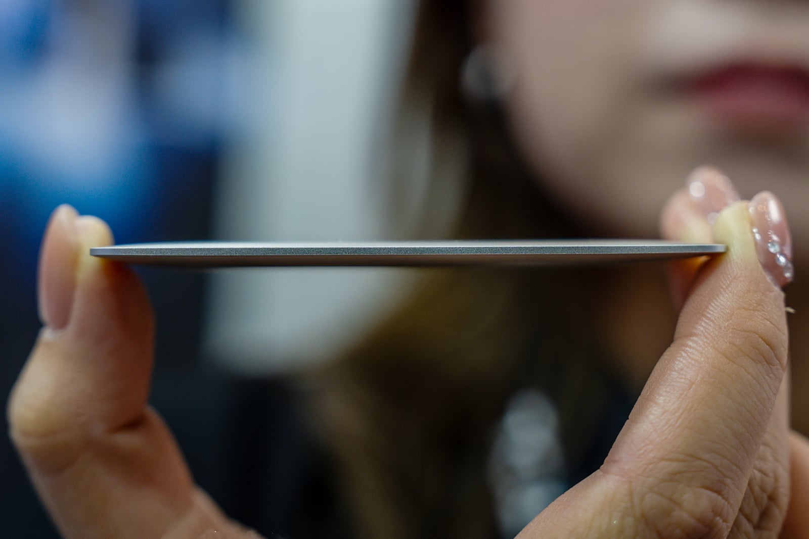 A person's hands hold a thin, circular metal disc with a tapered edge, viewed from the side.