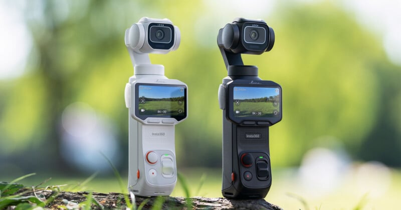 Two Insta360 gimbal cameras, one white and one black, stand side-by-side on a wooden surface against a blurred green background.