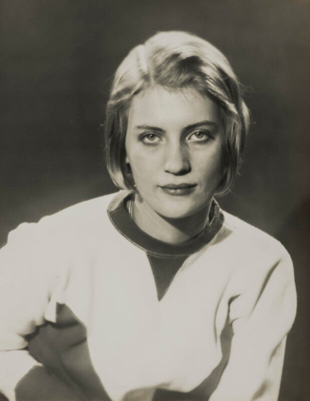 A black-and-white portrait of a young woman with short, light hair, wearing a light-colored sweatshirt with a dark V-neck insert.