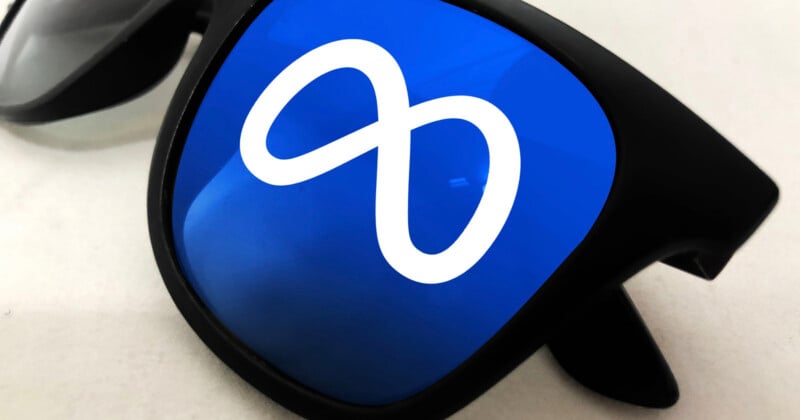 A pair of black sunglasses with the white Meta infinity logo reflected on the blue-tinted lens.