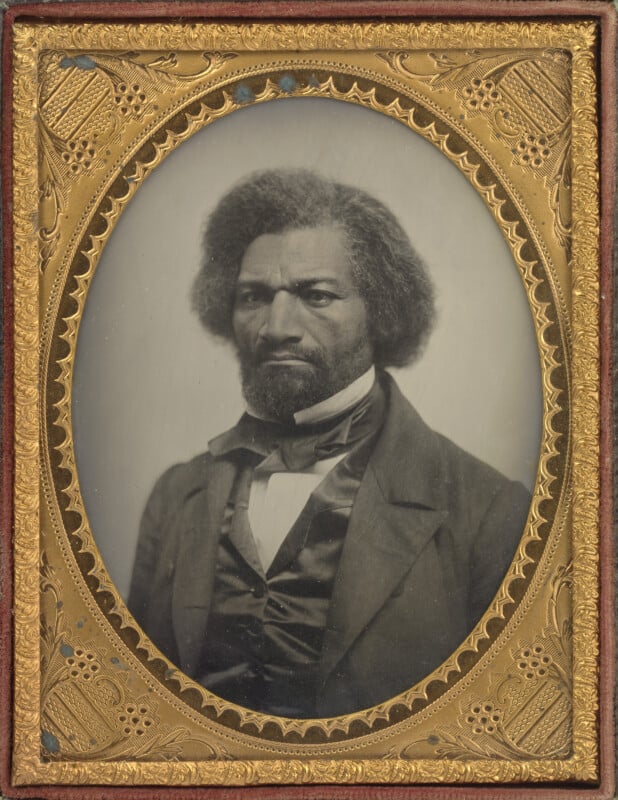 A daguerreotype portrait of Frederick Douglass, featuring his head and shoulders framed in an ornate, oval gold-colored border.