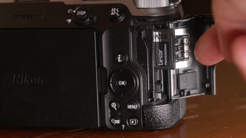 A person's finger pushes a Lexar Professional SD memory card into the side slot of a black Nikon camera.