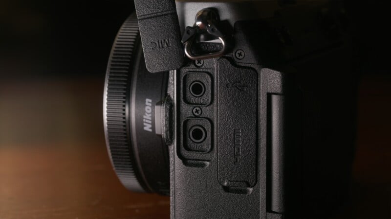 A close-up view of the side of a Nikon camera, showing open rubber port covers for microphone and headphone jacks, with a larger closed port cover labeled with USB and HDMI icons.
