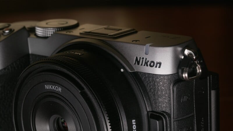 A close-up view of a silver and black Nikon Z fc mirrorless camera body with a Nikkor lens attached.