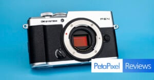 An OM SYSTEM PEN camera body with a silver top plate and black textured grip sits against a solid blue background.