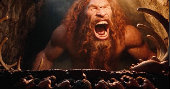 A giant, red-bearded cyclops roars at a group of armored warriors standing in a dark cave.