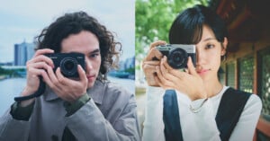 Two people hold OM SYSTEM PEN cameras up to their faces in a side-by-side portrait.
