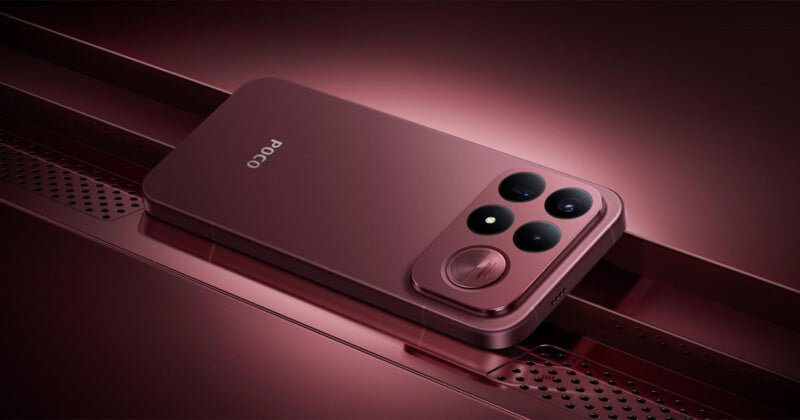 A dark red smartphone with a triple-camera array and a circular speaker grille rests on a matching metallic surface with a perforated pattern.