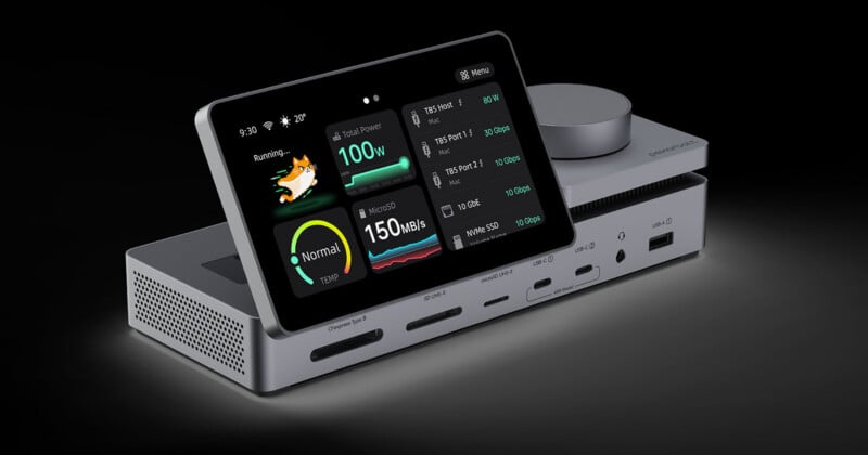 A metallic docking station with a built-in touchscreen display showing system status, ports, and a pixel-art cat, featuring various card slots and USB ports on the front panel.