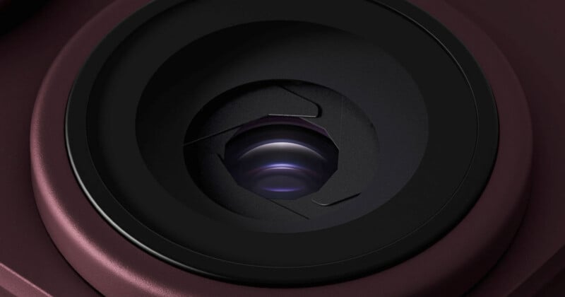 A close-up view of a camera lens with a partially closed mechanical aperture, surrounded by a dark maroon housing.