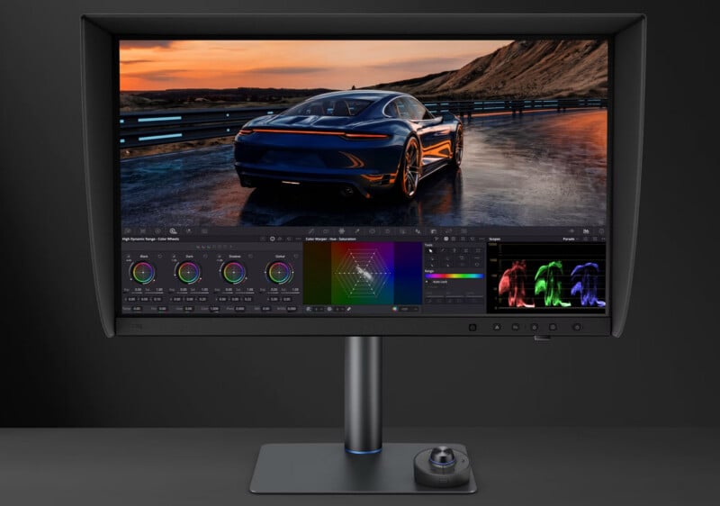 A professional monitor with a shading hood displays color grading software on a desk with a circular control dial.