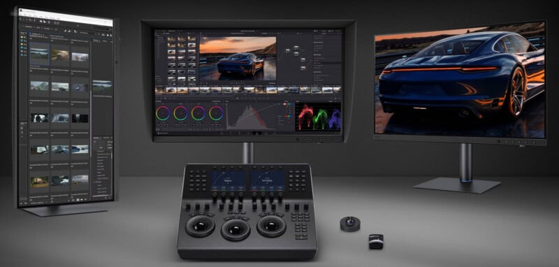 A professional video editing workstation featuring a vertical monitor, a central color grading monitor with a hood, a right-hand display showing a car, and a control console with trackballs and knobs.