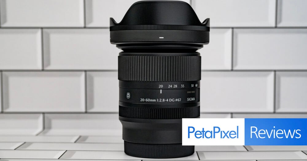 A Sigma 20-60mm f/2.8-4 DG lens stands upright against a white tiled background, with a PetaPixel Reviews logo in the bottom right corner.