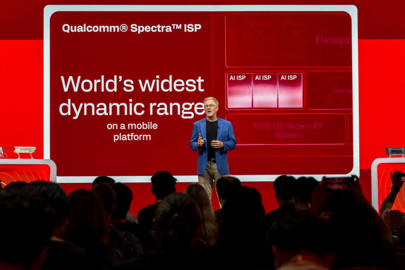 A man in a blue blazer stands on a stage in front of a large screen displaying "Qualcomm Spectra ISP" and "World's widest dynamic range on a mobile platform" to an audience.