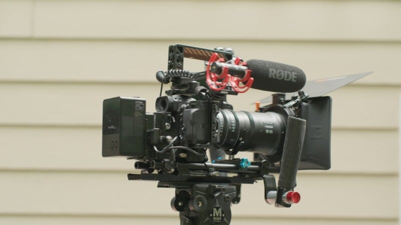 A professional cinema camera rig mounted on a tripod, featuring a Fujinon lens, a Rode microphone, a matte box, and a V-mount battery.