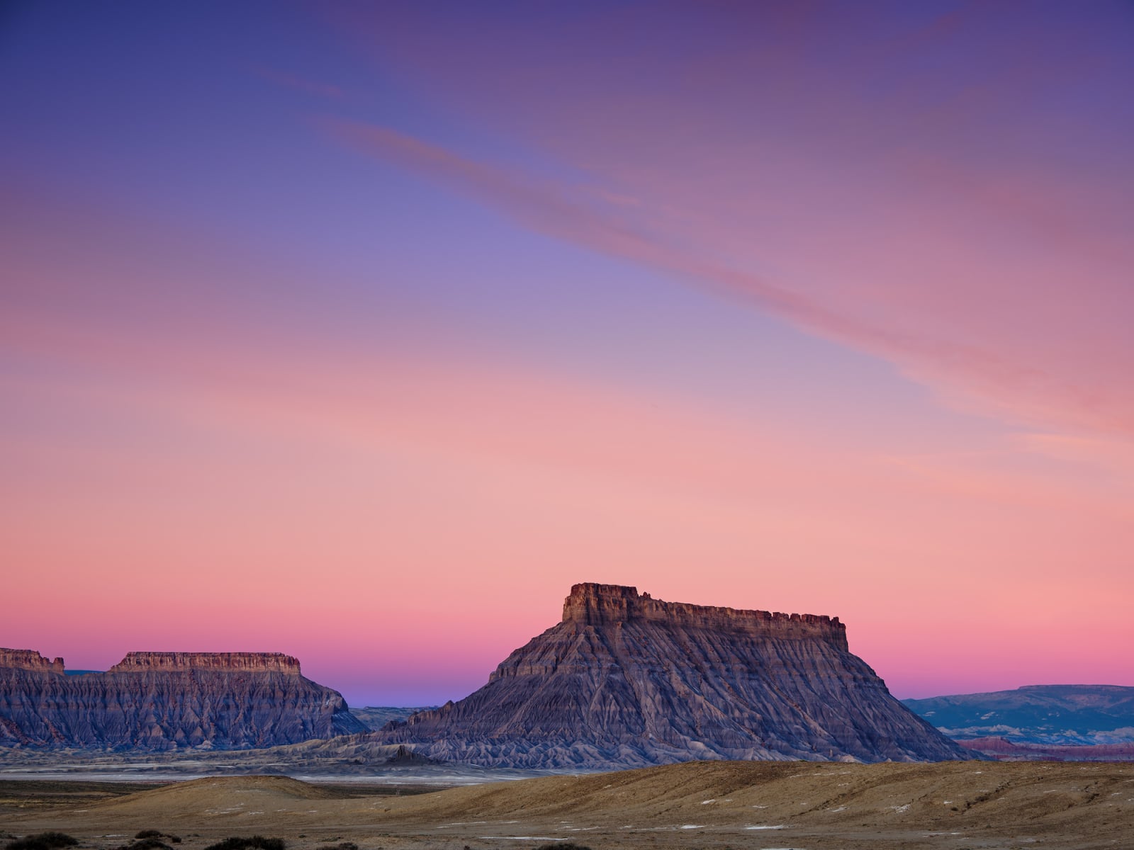 Two large, flat-topped mesas rise from a desert landscape under a vibrant pink and purple sunset sky.