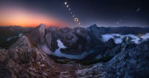 A composite view of a solar eclipse over a winding river valley surrounded by jagged, rocky mountains at twilight.