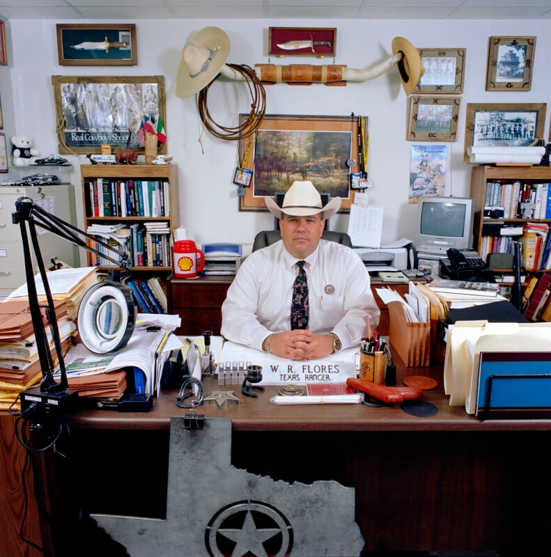 Texas Ranger W. R. Flores sits at his desk in an office decorated with western memorabilia, framed photos, and a large metal Texas-shaped sign.