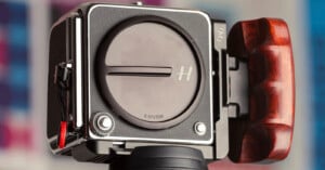 A close-up view of a medium format camera body with a lens cap labeled "X SYSTEM" and a wooden handgrip attached to the side.