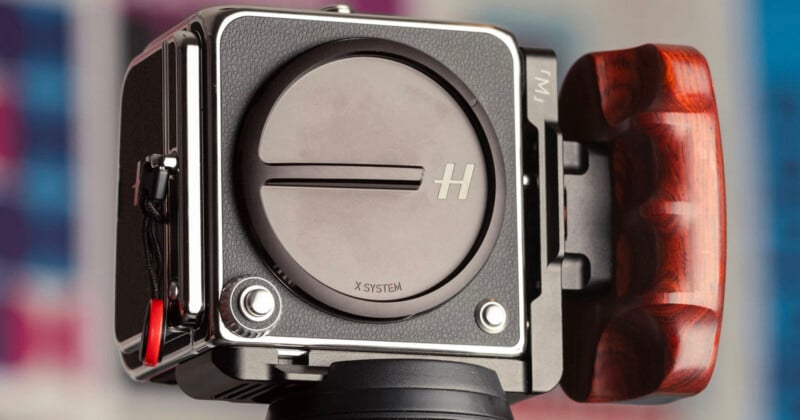 A close-up view of a medium format camera body with a lens cap labeled "X SYSTEM" and a wooden handgrip attached to the side.