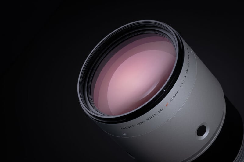 A close-up, angled view of a silver camera lens against a black background, with text on the barrel reading "FUJINON LENS SUPER EBC XF 400mm 1:4.5 R LM OIS WR".
