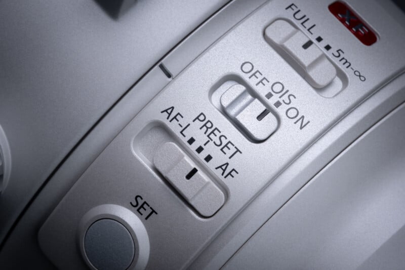 Close-up of a camera lens barrel showing three switches labeled FULL/5m-∞, OIS OFF/ON, and AF-L/PRESET/AF, along with a SET button.