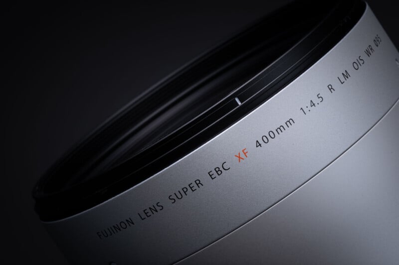A close-up, angled view of a silver camera lens barrel against a dark background, showing the text "FUJINON LENS SUPER EBC XF 400mm 1:4.5 R LM OIS WR 095".