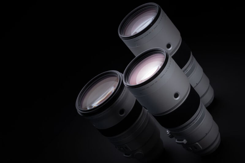 Three silver telephoto camera lenses are arranged diagonally against a black background.