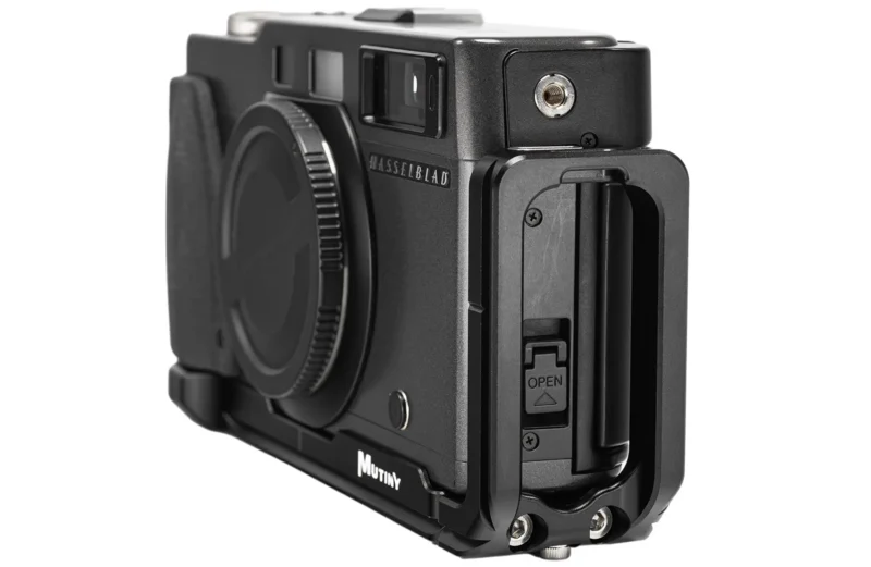 A black Hasselblad camera body fitted with a black Mutiny metal cage, shown from a front-side angle against a white background.