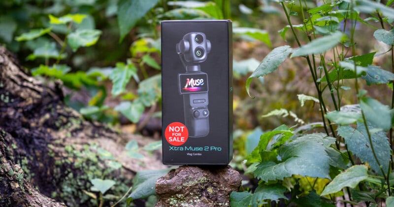 A black product box for an "Xtra Muse 2 Pro" vlog combo sits on a tree stump in a wooded area, featuring a "NOT FOR SALE" sticker.